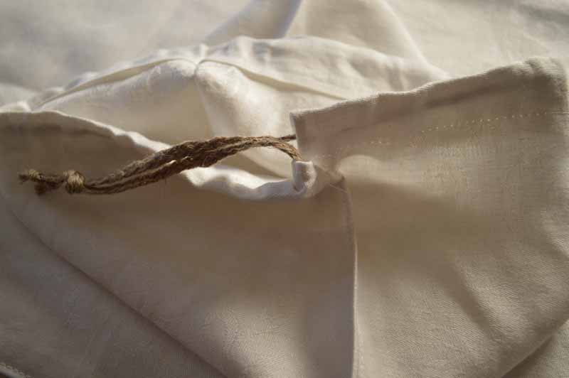 Did you know that storing bread in a linen bag can make it last longer? Here's how to make one in 15 minutes! Bonus: You'll eliminate some plastic bags from the landfill. 用棕色亚麻麻绳面包袋的开口边的特写储存自制的面包