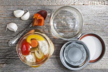 home canning in process: empty canning jar and a canning jar full of vegetables with lids on the table