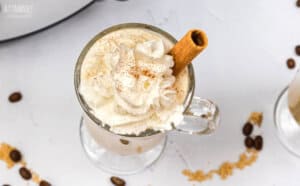 glass mug with a drink, topped with whipped cream and a cinnamon stick