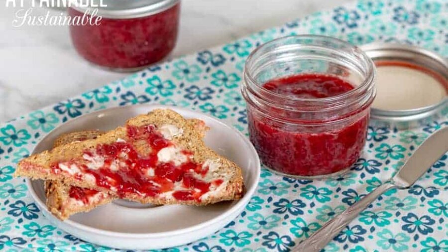 two jars of strawberry compote on a teal napkin with pieces of toast buttered and spread with compote